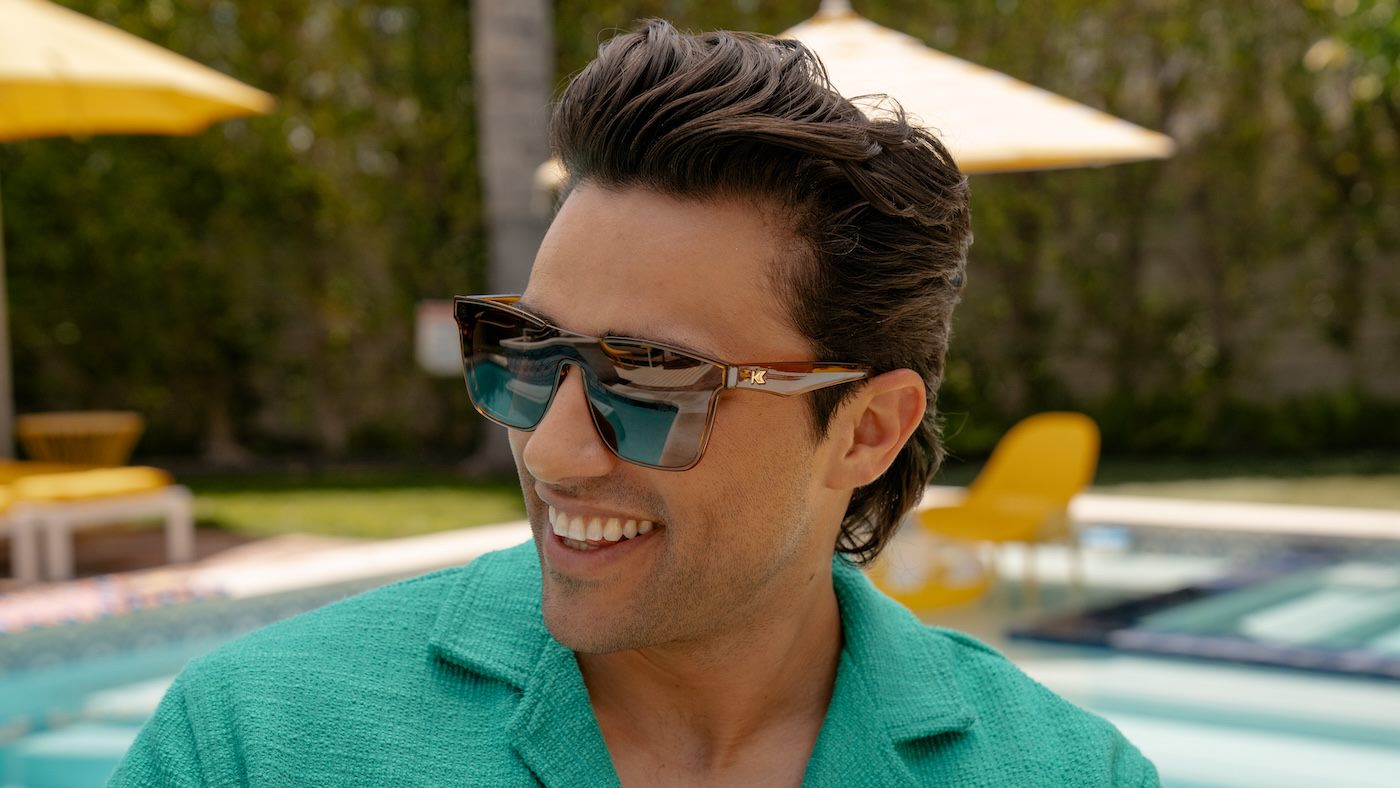 Man wearing Rio Afters sunglasses and a green shirt by a poolside with yellow umbrellas.
