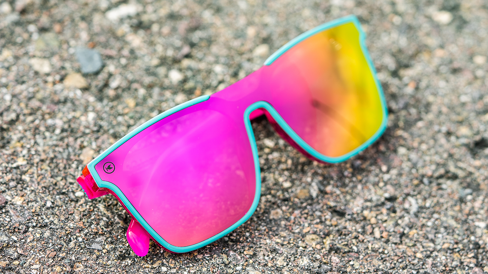 Sunglasses with a teal and pink frame with polarized pink and purple lenses, flyover